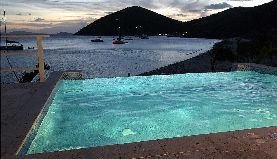 Dusk over White Bay from the pool at Pink House Villas, above the east beach: boats at anchor and lights along the main beach under the hill at the west end (2019)