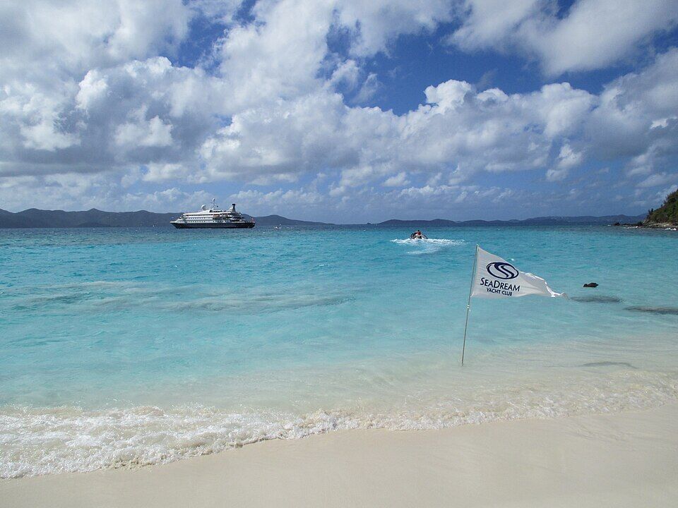 A SeaDream Yacht Club flag planted in the shallows at White Bay, with the SeaDream II at anchor offshore (February 2015)
