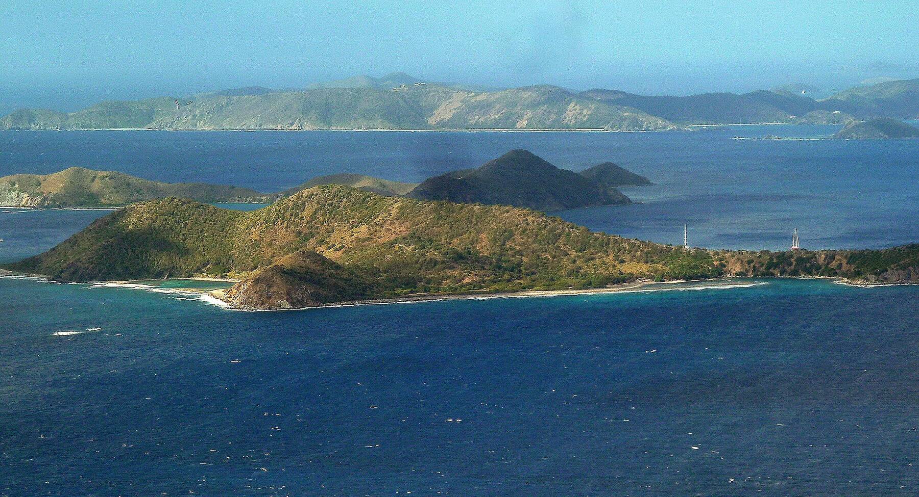 Cooper Island from the air, its green hills and sandy shore ringed by reef, with Salt Island and Peter Island beyond and Tortola across the channel
