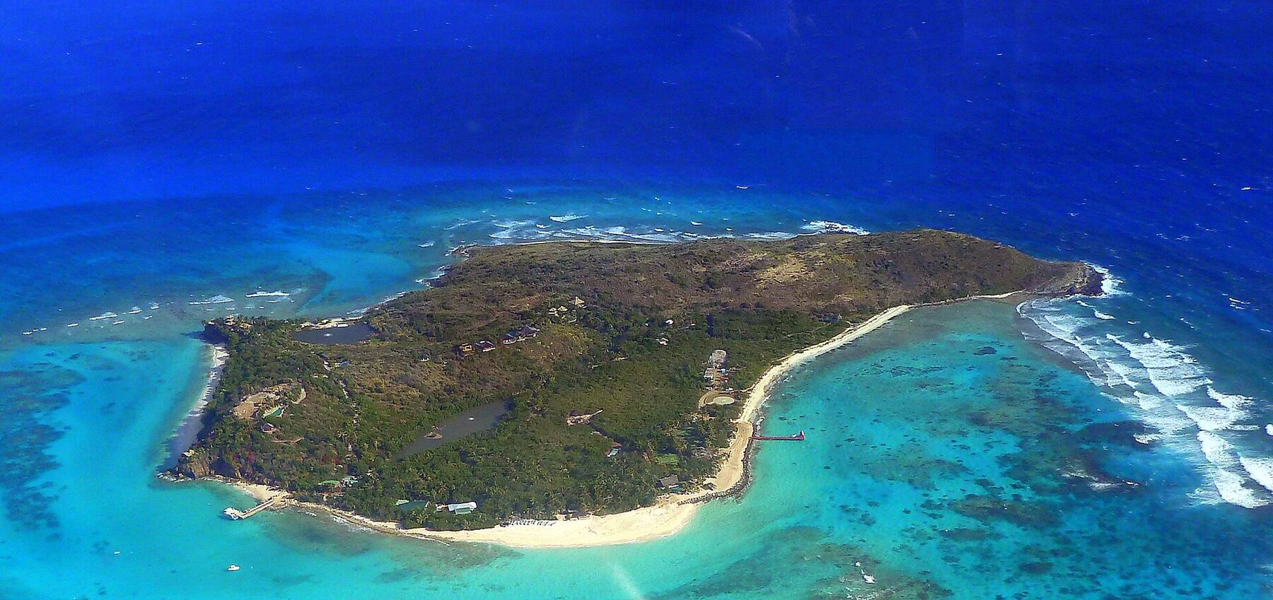 Necker Island from the air: the wooded island ringed by reef, the long beach and the guests' jetty on its south-east side, and the open Atlantic beyond