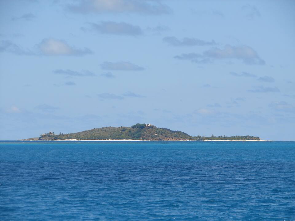 Necker Island seen from a boat at a distance: a low green island with the Great House on its hill
