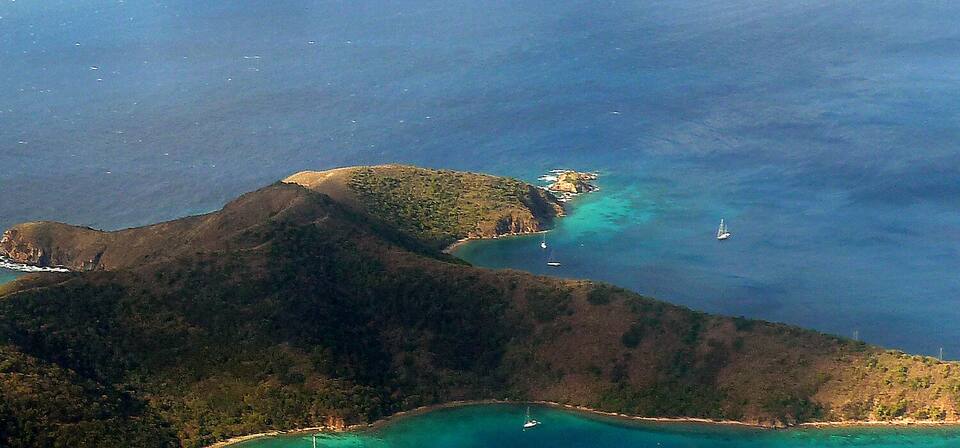 The west end of Norman Island from the air: dry, scrub-covered hills, turquoise coves and yachts at anchor