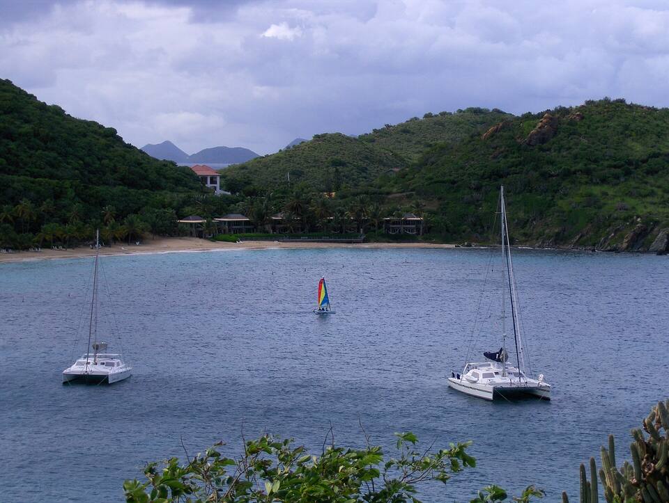 Two catamarans and a small sailboat on moorings off Deadman's Beach, with the beach and the hills of Peter Island behind