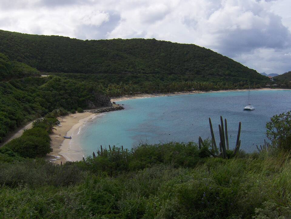 Deadman's Bay from the hill above Sprat Bay: a small beach and the path in front, the long sweep of Deadman's Beach beyond and a catamaran on a mooring