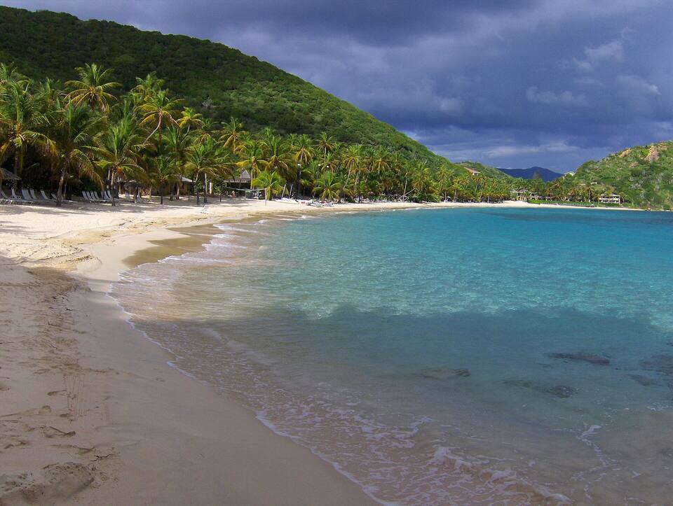 Deadman's Beach, Peter Island: a crescent of sand under coconut palms and green hills, with clear shallow water