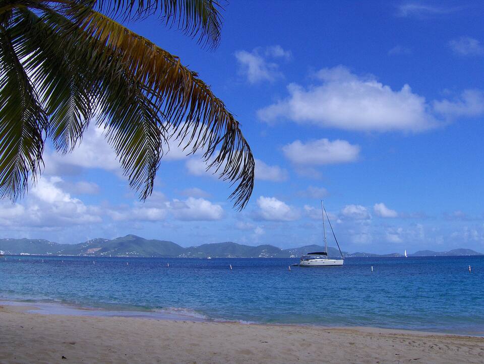 From Deadman's Beach under a palm frond: a yacht at anchor and Tortola across the Sir Francis Drake Channel