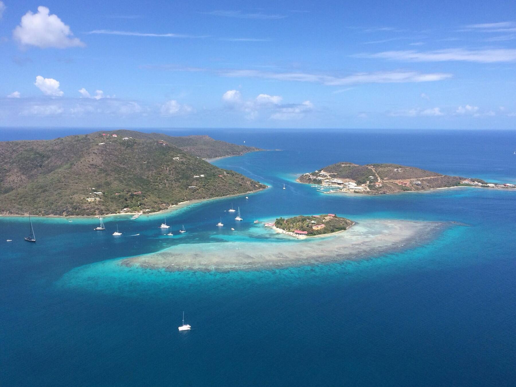 From the air: Marina Cay on its reef in front, Scrub Island with the resort and marina on the right, Great Camanoe on the left and yachts on the moorings between