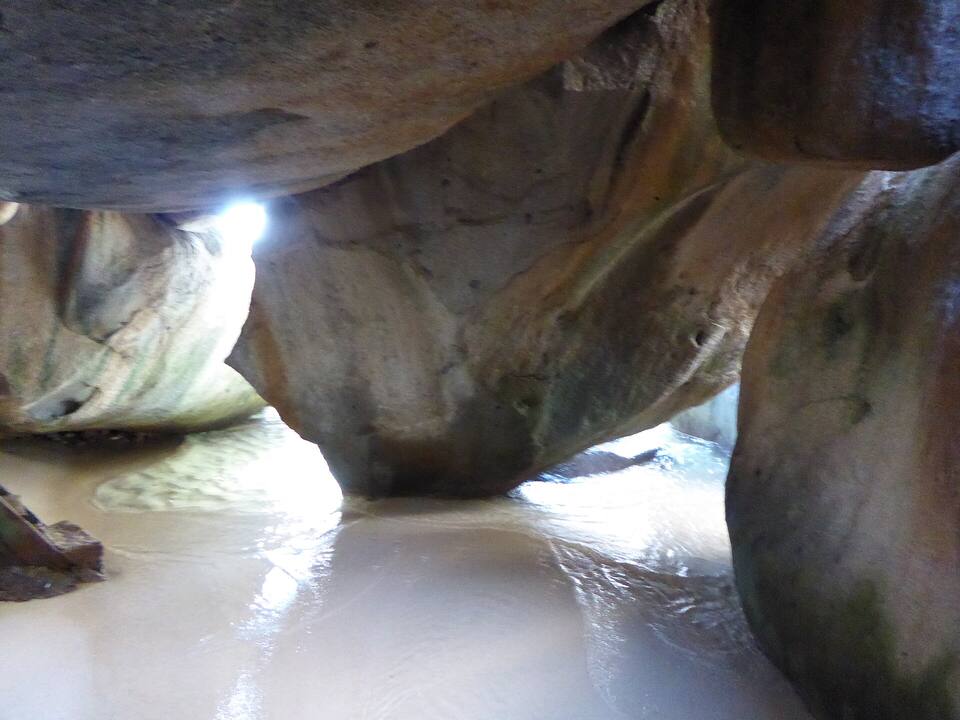 Inside a grotto on the Caves trail at The Baths: sand floor, daylight through the boulders